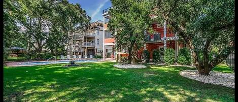 A two-story building with a swimming pool, surrounded by lush greenery and trees.