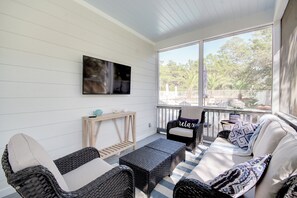A sunlit porch with wicker furniture, a TV, and a view of trees.