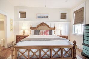 A bedroom with a wooden bed, two bedside tables with lamps, a dresser, and a framed picture on the wall.