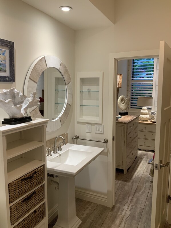 A bathroom with a white sink, a round mirror, a small cabinet, wicker baskets, and a wooden floor.