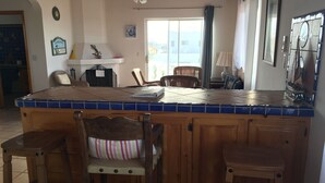 Une cuisine avec un îlot central recouvert de carreaux, des chaises en bois et un ventilateur de plafond.