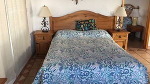Une chambre à coucher avec une tête de lit en bois, une couvre-lit à motifs floraux, deux tables de chevet avec des lampes et un élément décoratif mural.