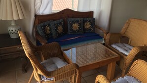 Une pièce chaleureuse avec un canapé en bois, deux fauteuils en osier, une petite table et une lampe.