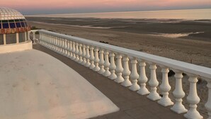 Un balcon doté d’une balustrade blanche, donnant sur un paysage plat et une structure en forme de dôme.