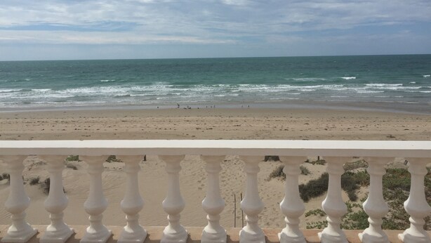 Une vue sur la plage, avec les vagues, une étendue de sable et la rambarde d’un balcon.