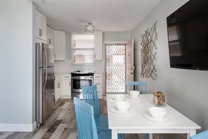 Enjoy meals at the dining table, set with white plates and bowls, in this kitchen featuring a refrigerator, oven, and television.