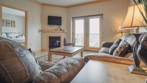 A living room with a fireplace, a television mounted on the wall, and a balcony with a view. - Base Camp - Unit 1305 - Mountain View Condos - FREE Attraction Ticket with EACH night Stay Including Dollywood (Pigeon Forge)