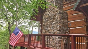 Una cabaña llamada Treetop Cabin con una chimenea de piedra, una terraza de madera y una bandera estadounidense.