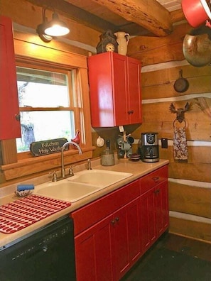 A kitchen with a sink, red cabinets, a window, and various kitchen items.