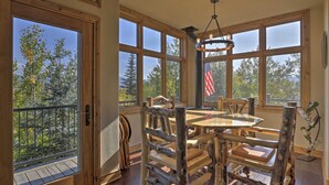 A dining area with a wooden table and chairs, large windows with a view of trees, and an American flag. - 7 Mi to Copper Mtn: Condo w/ Deck & Stunning Views (Frisco)