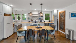 A modern kitchen with white cabinets, a wooden dining table, and pendant lighting.