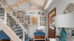 A staircase with a wooden finish, a bench with a blue cushion, and a wall with framed nautical-themed artwork.