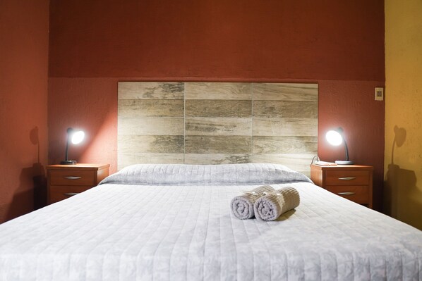 Una cama bien tendida con toallas enrolladas, dos mesitas de noche con lámparas y un cabecero de madera.