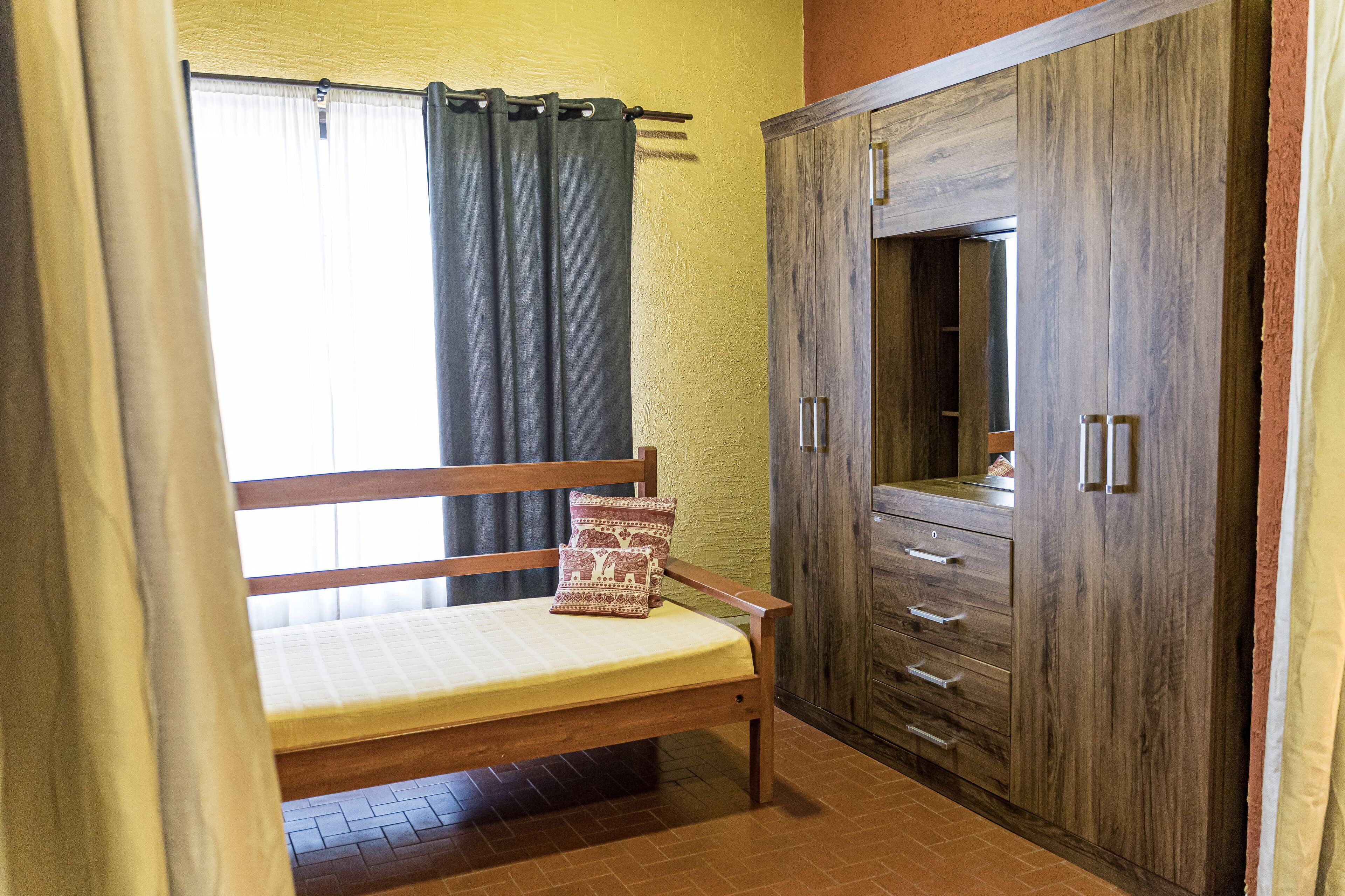 Une pièce avec un lit, une armoire en bois et une fenêtre avec des rideaux.