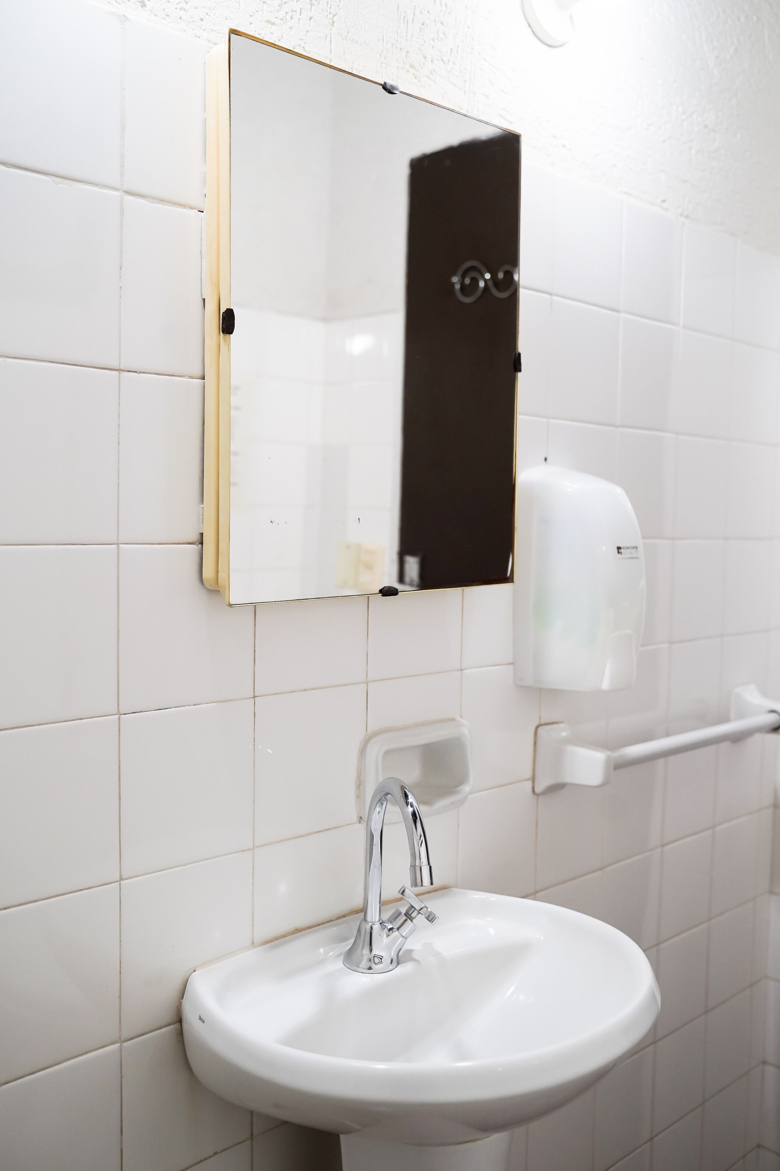 Un bagno con un lavandino bianco, uno specchio e un dispenser di sapone.