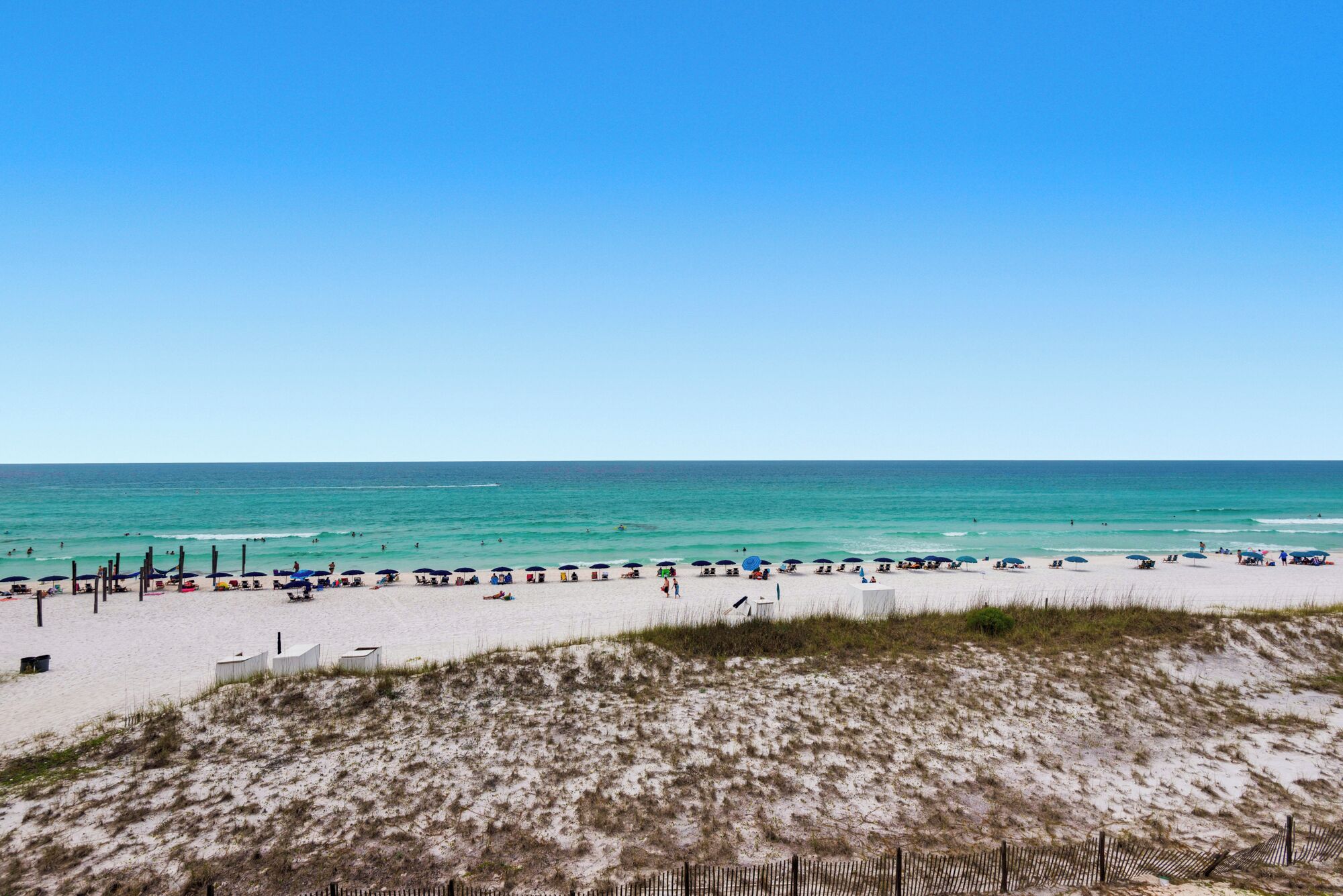 Une plage de sable blanc, avec une eau d’un bleu limpide et quelques parasols.
