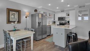 A modern kitchen with a central island, stainless steel appliances, and a dining area with a table and chairs. - BeachFront, Bch Svc, pool, wifi, Kitchen, grill (Destin)