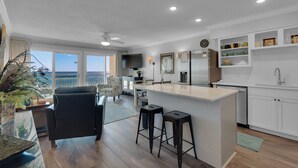 A modern kitchen with a central island, bar stools, a dining area with a view, and a large window overlooking the ocean. - BeachFront, Bch Svc, pool, wifi, Kitchen, grill (Destin)