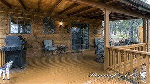 A wooden cabin with a covered porch, a grill, and seating areas.