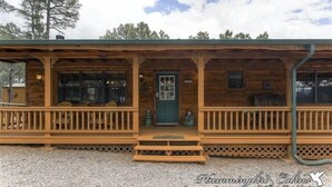 A rustic log cabin with a porch, a green door, and a small window.