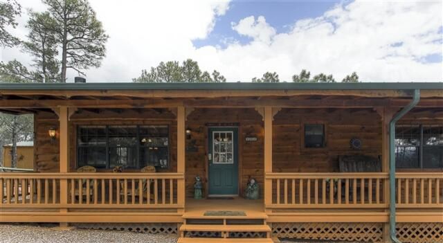 A rustic log cabin with a porch, a green door, and a small window.