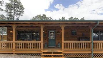 A rustic log cabin with a porch, a green door, and a small window.