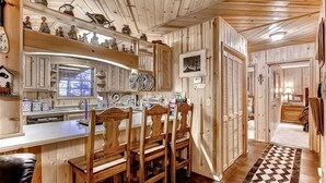 A wooden interior with a kitchen area featuring a bar, wooden chairs, and shelves with decorative items.