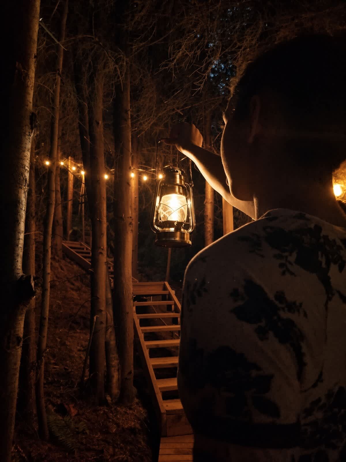 A wooden staircase leading up to a lantern-lit area surrounded by trees.