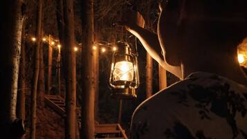 A wooden staircase leading up to a lantern-lit area surrounded by trees.