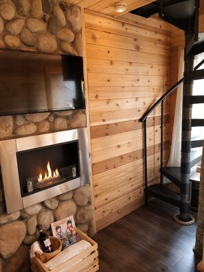 Een houten interieur met een stenen muur, een open haard, een trap en een houten bankje met een fles en een boek.