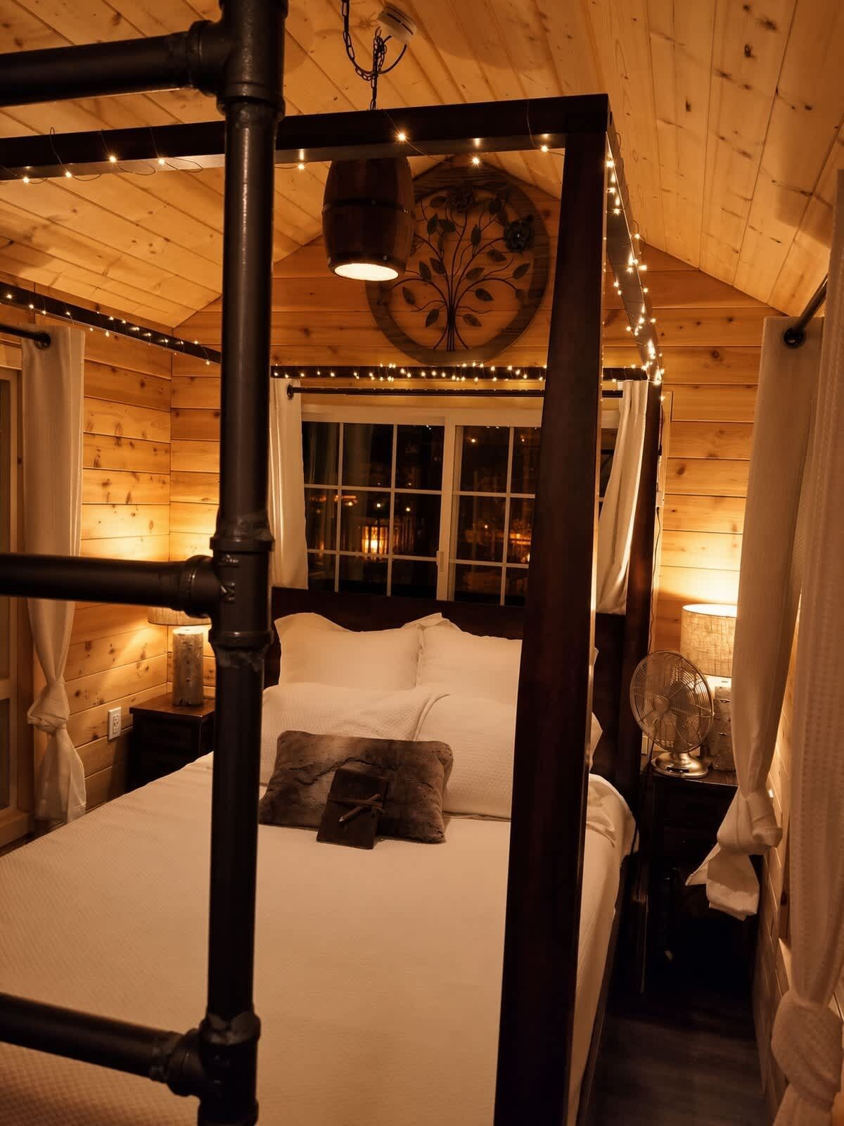 Een hemelbed met baldakijn, een nachtkastje met een lamp en een ventilator bevestigd aan de muur.