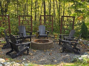 A circular fire pit surrounded by four Adirondack chairs, set on a gravel surface with a wooden fence and trees in the background. - Treehouse Place at Deer Ridge Featured top 10 USA (Snohomish)