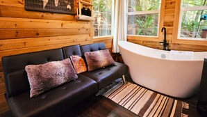 Interior de una cabaña con un sofá de cuero negro, una bañera grande y un mapa mundial en la pared.