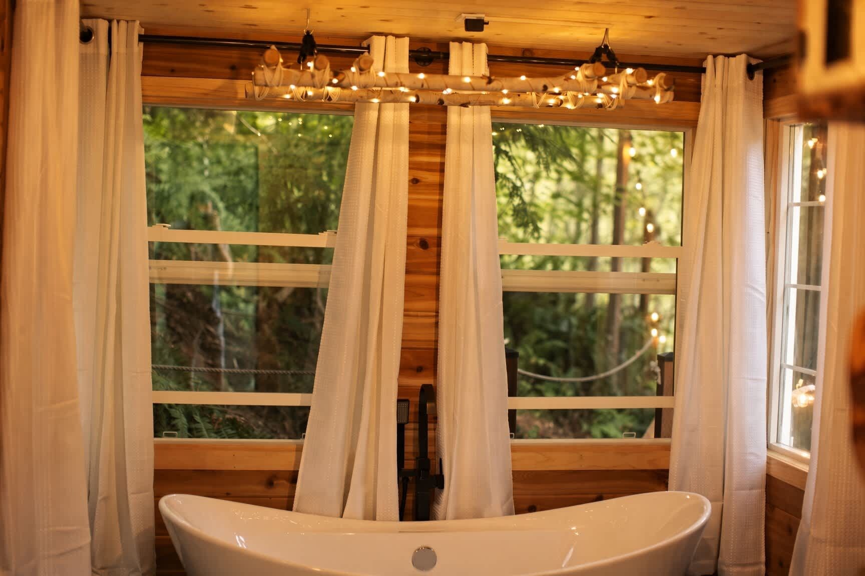 Ein Holzblock-Interieur mit großem Fenster, Vorhängen und einer Badewanne.
