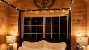 Un dormitorio rústico con cabaña de madera, una cama grande, dos lámparas de noche, un ventilador de techo y luces colgantes.