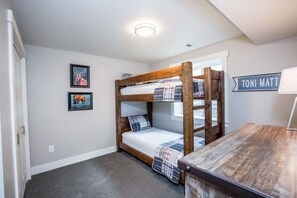 Une chambre avec un lit superposé, une tête de lit en bois, un petit bureau et une pancarte sur laquelle on peut lire « TONI MATT ».