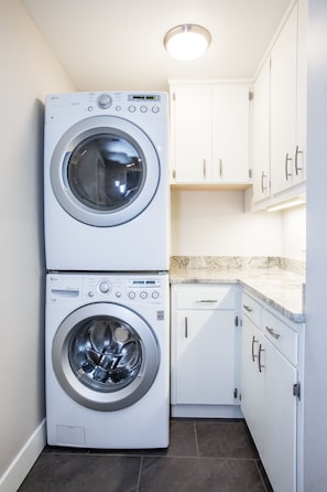 A laundry room with two stacked front-loading washing machines, white cabinets, and a marble countertop.