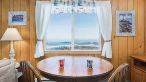 Um quarto com parede revestida de madeira, uma mesa redonda de madeira com duas canecas, um abajur e um quadro com uma imagem de um farol.