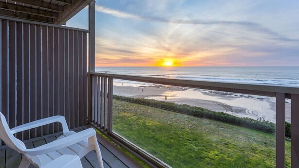 Varanda com cadeiras brancas com vista para uma praia ao pôr do sol.