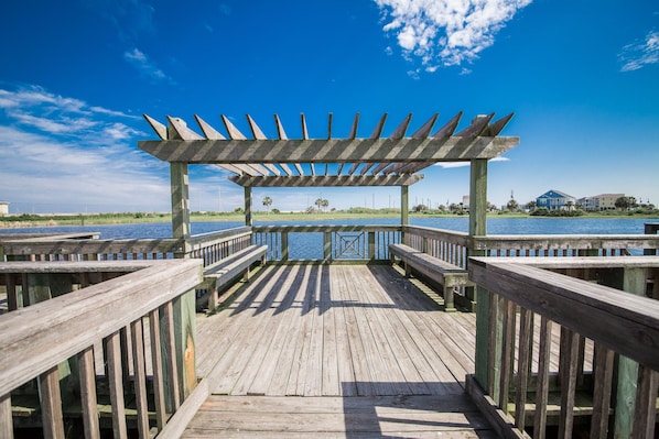 Un muelle de madera que conduce a un mirador con vistas al agua y edificios lejanos.