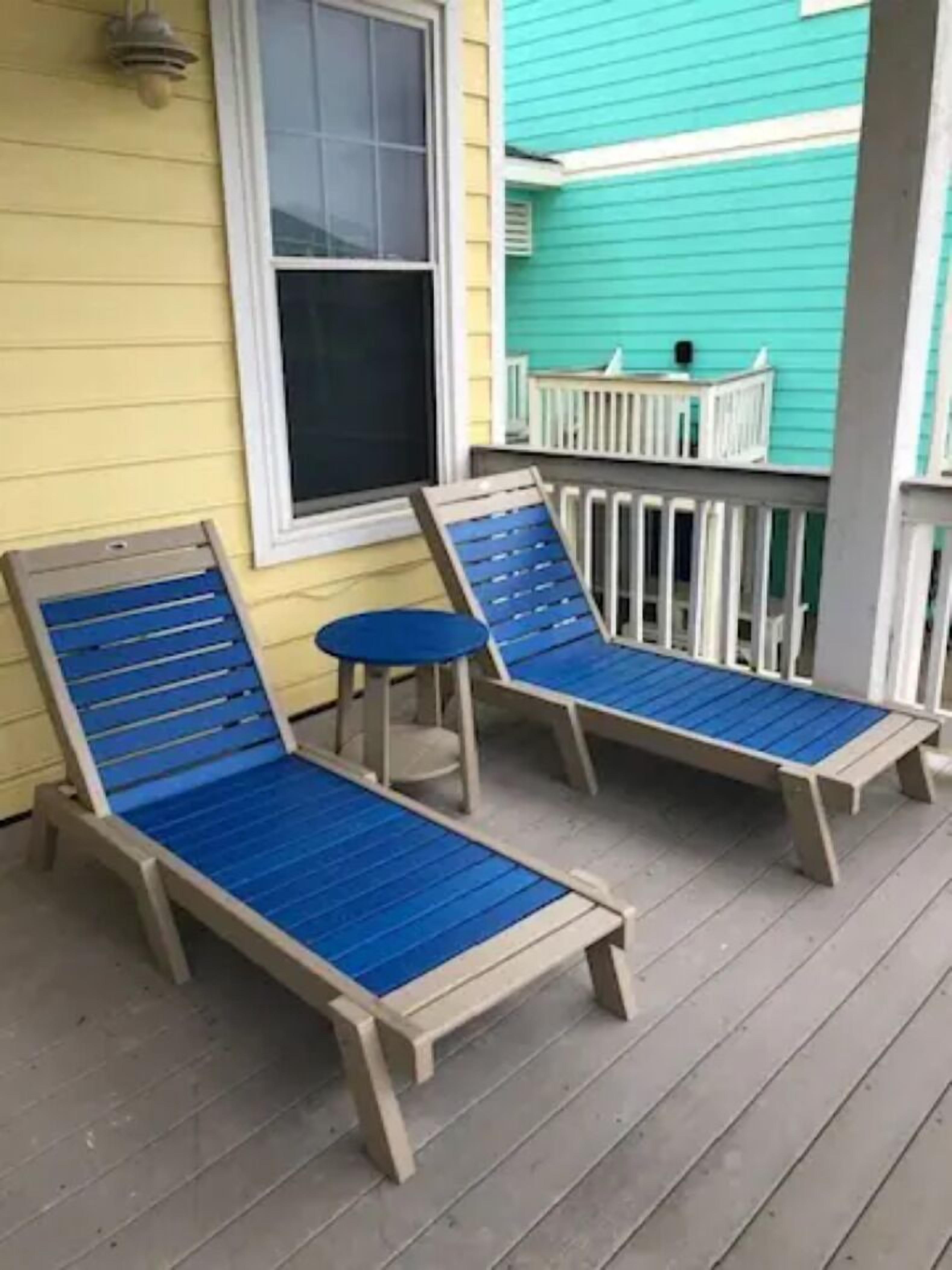 Deux fauteuils bleus avec des structures en bois, placés sur une terrasse en bois, une petite table ronde et une rambarde blanche.