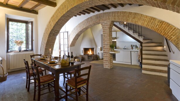 A spacious dining area with a brick archway leading to a kitchen and a staircase.