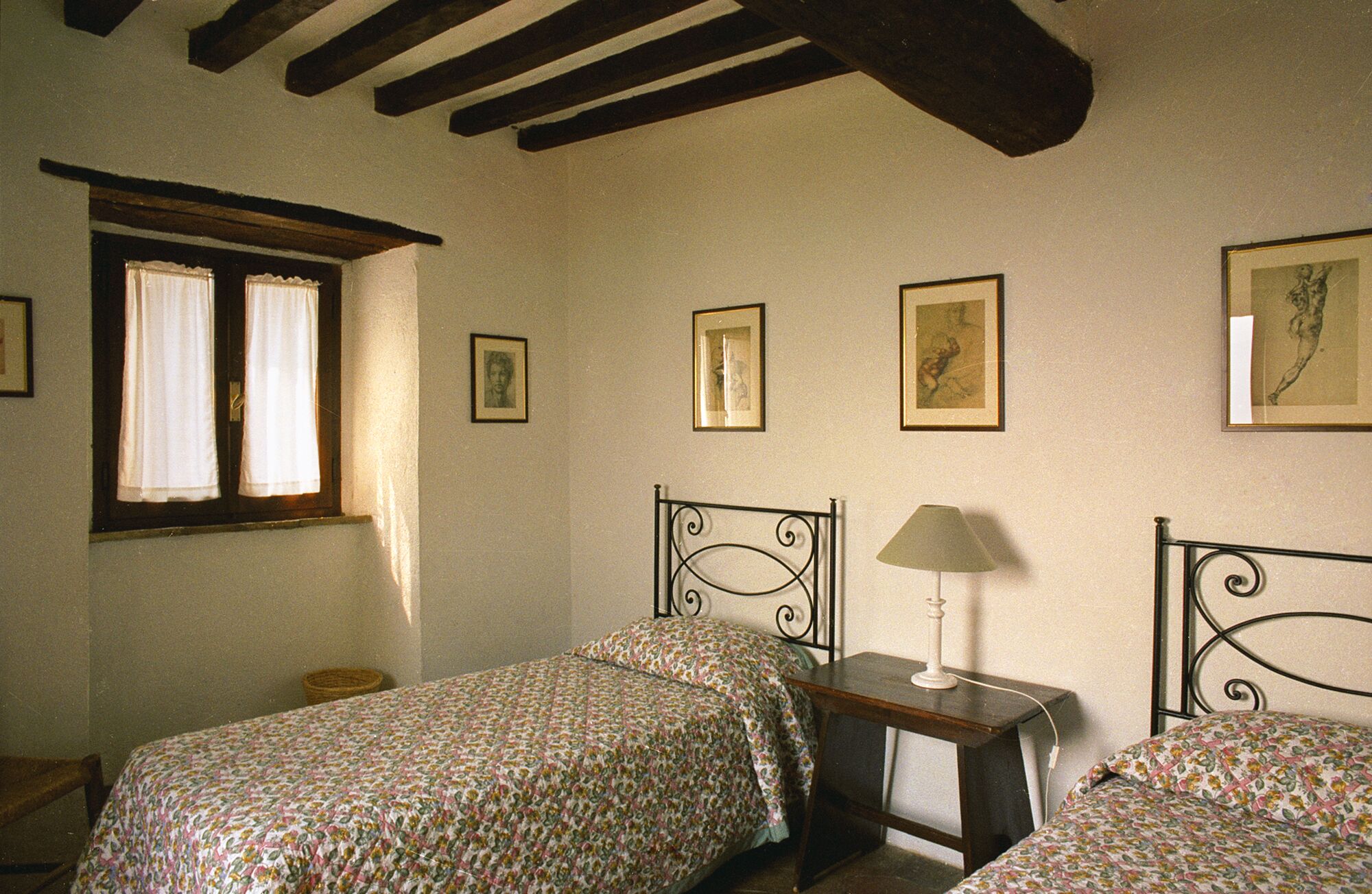 A bedroom with two beds, a window with curtains, and several framed pictures on the wall.