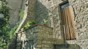 A stone building with a rustic appearance, featuring a small staircase leading to a door with a metal gate.
