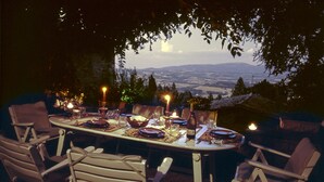 An outdoor dining area with a table set for six, surrounded by chairs, and overlooking a scenic landscape.