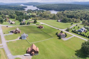 An aerial view of a rural area with multiple houses, a large open field, and a lake in the background.