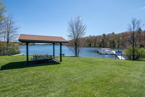 A lakeside gazebo with a picnic table, surrounded by a grassy area and trees.