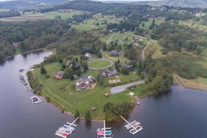An aerial view of a lakeside property with multiple houses, a circular driveway, and a dock with boats.