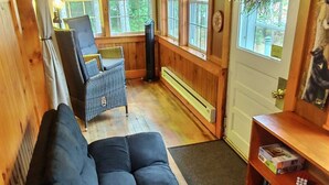 En mysig stuga med en mörk soffa, en fåtölj, en bokhylla och en dörr som är dekorerad med en krans.