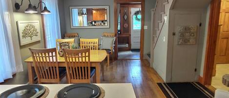 Comedor con mesa y sillas de madera, un candelabro y vista a la cocina.